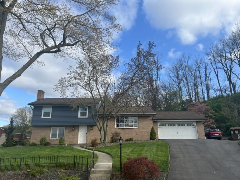red brick home with two car garage and second story with blue siding in Avon, PA