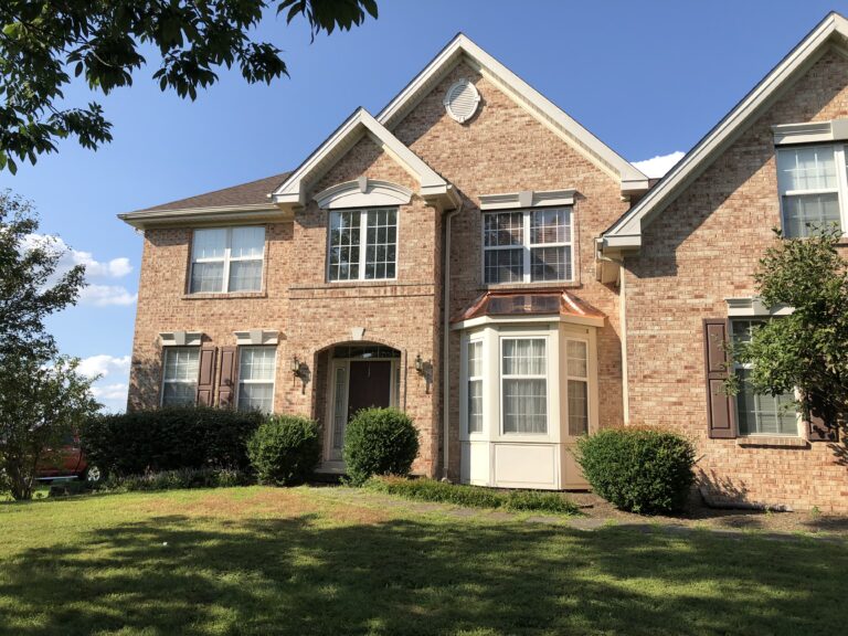 Red brick home with white window well with red copper roofing in Jonestown, PA